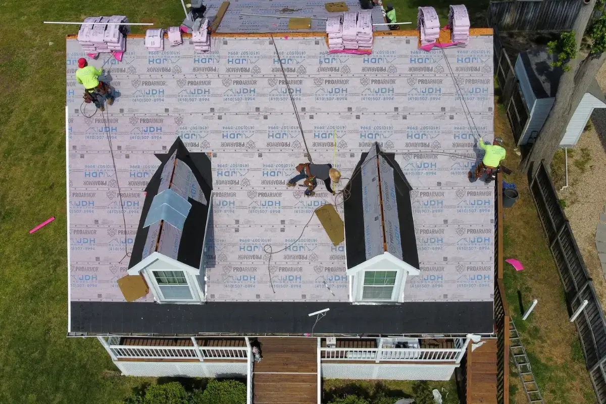 Aerial view of an active roof replacement on a Lexington Park Maryland residential home showing two dormers, protective sheathing, and contractor crew working