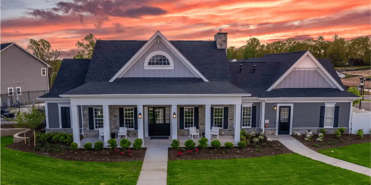 JDH Remodeling newly completed two-story colonial Port Republic Maryland home with white vinyl siding, dark asphalt shingle roof, front portico, and replacement windows in a wooded setting