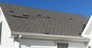 Asphalt shingle roof with multiple missing shingles, showing exposed areas vulnerable to water leaks.