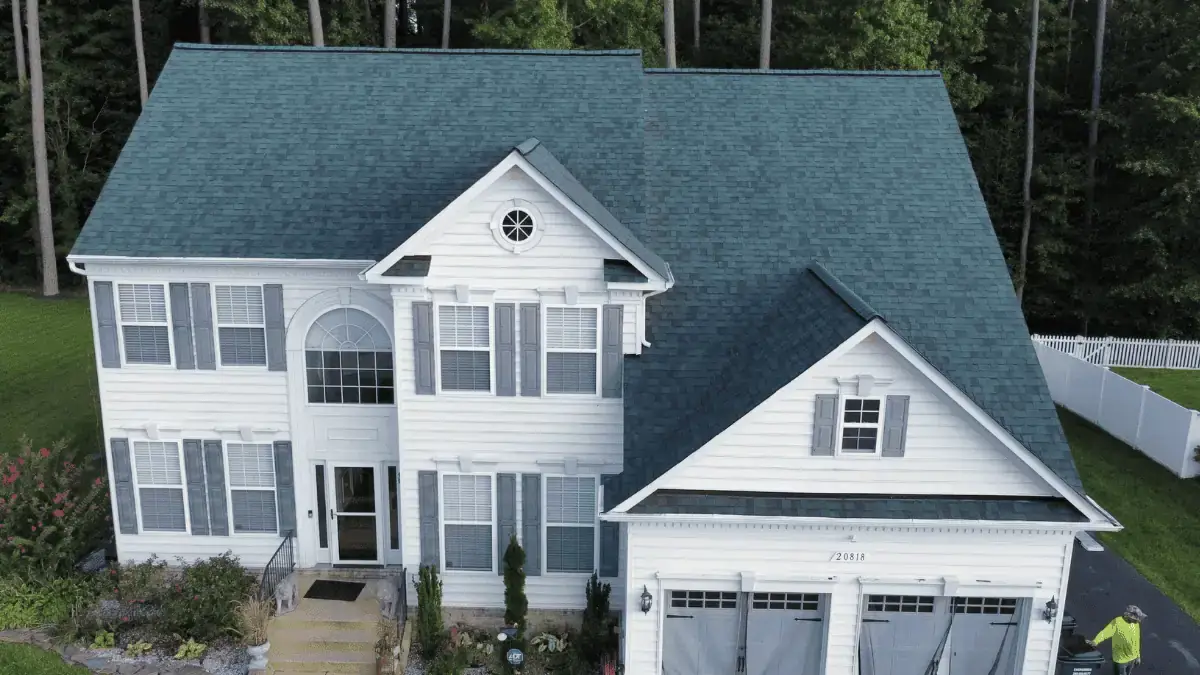 JDH Remodeling two-story white colonial home in the Anne Arundel County corridor with new blue-gray asphalt roof, white siding, and four-car garage doors representing Crofton estate-tier housing