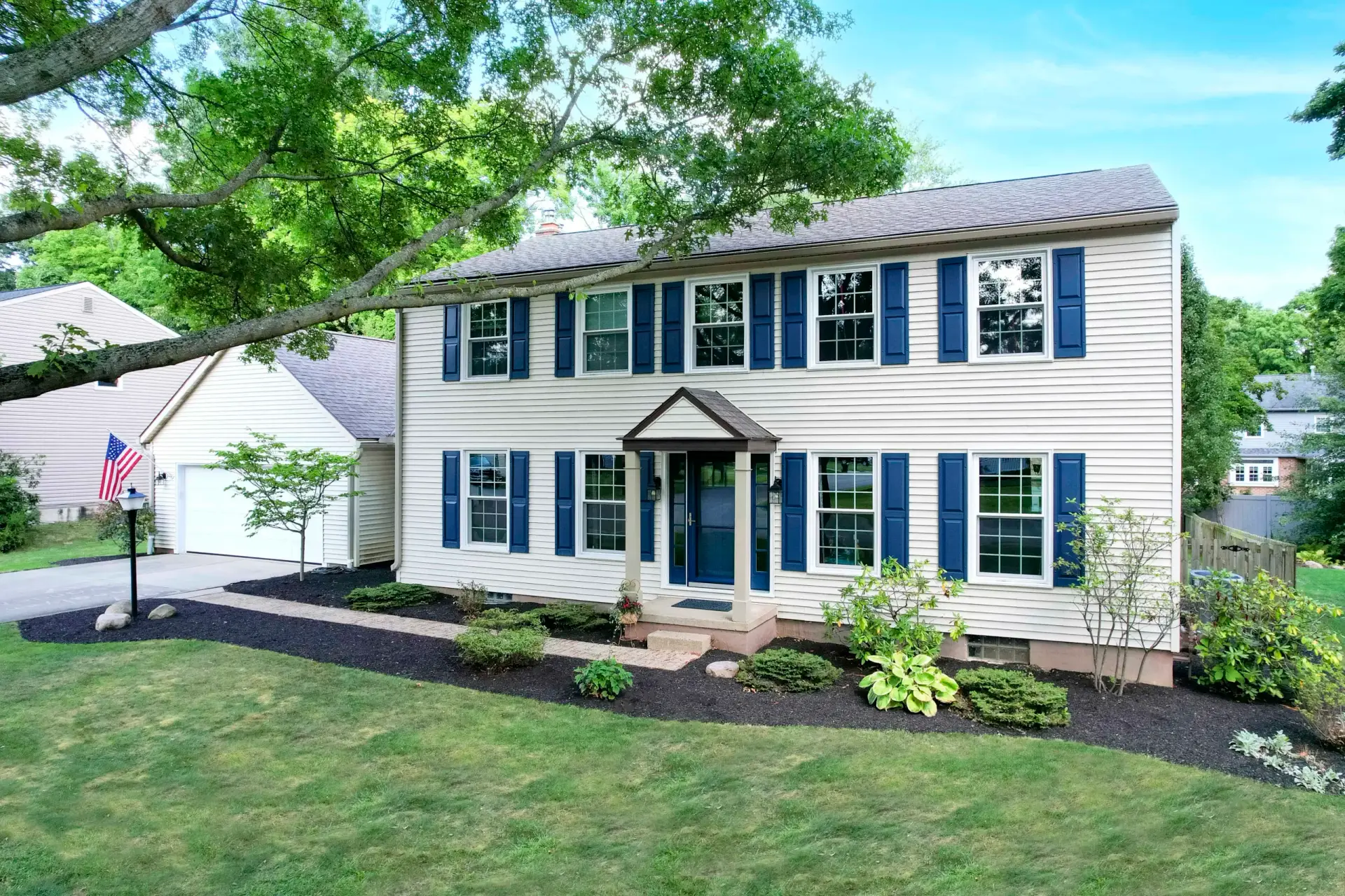 JDH Remodeling colonial home exterior featuring white vinyl siding, navy blue shutters and trim, multiple replacement windows, brick foundation, and professional landscaping on a Fredericksburg Virginia home