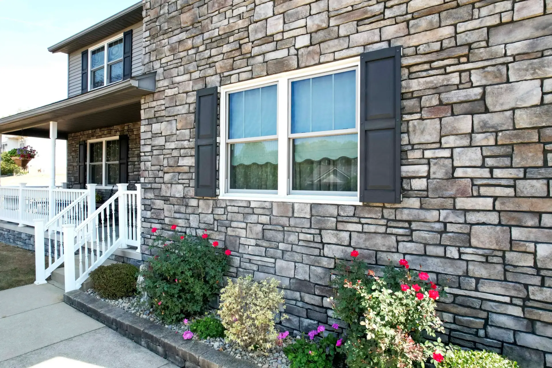 JDH Remodeling modern stone home exterior showcasing new white-frame replacement windows with dark shutters and landscaping on a Fredericksburg Virginia home