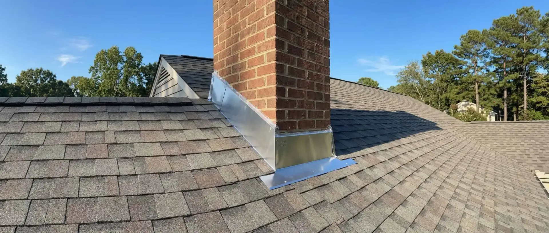 Completed JDH roof repair in Southern Maryland showing valley flashing with new shingles and metal trim around chimney