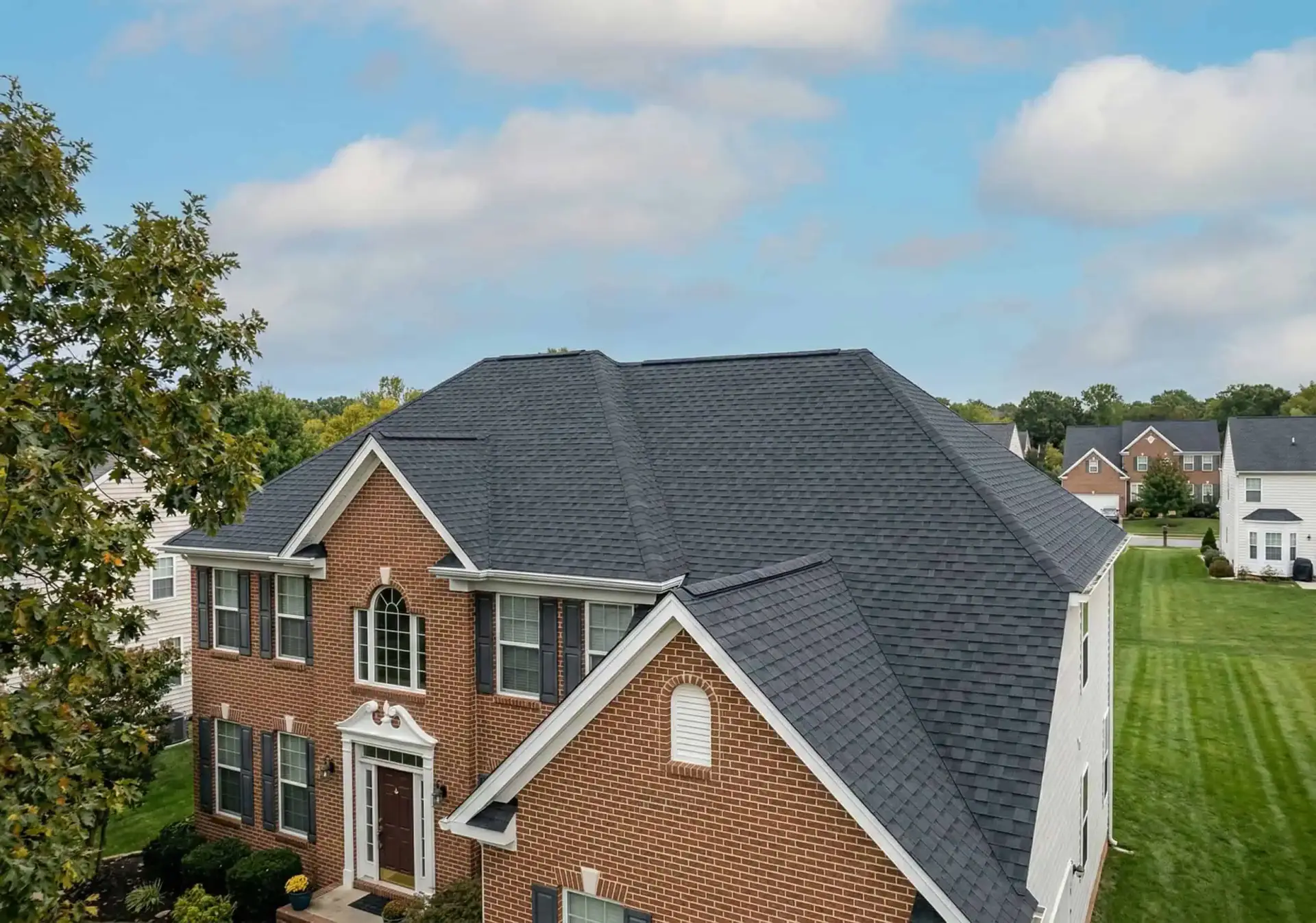 Completed JDH Remodeling roof replacement on a two-story Maryland home — new dark charcoal Owens Corning Duration architectural shingles with clean ridge line and full gutter system